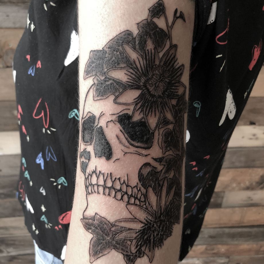 Tatuaje black work de una calavera rodeada de hiedra y flores de la pasión